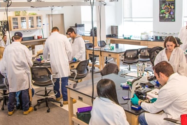 Biology lab filled with JWU students in lab coats.