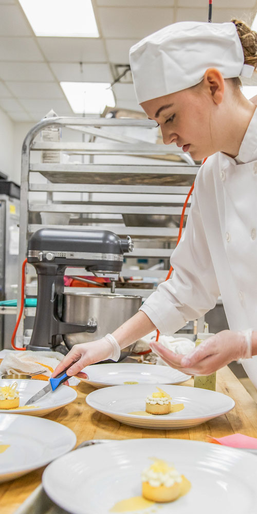 Student plating multiple plates in a culinary kitchen. 