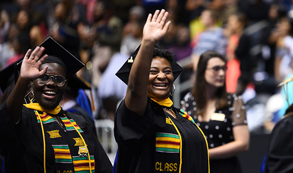 Two graduates waving to their family at commencement