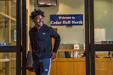 Student walking out of "Cedar Hall North" smiling