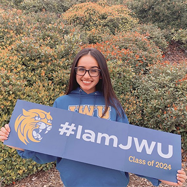 Student holding up their #iamjwu accepted student banner and wearing a JWU sweatshirt
