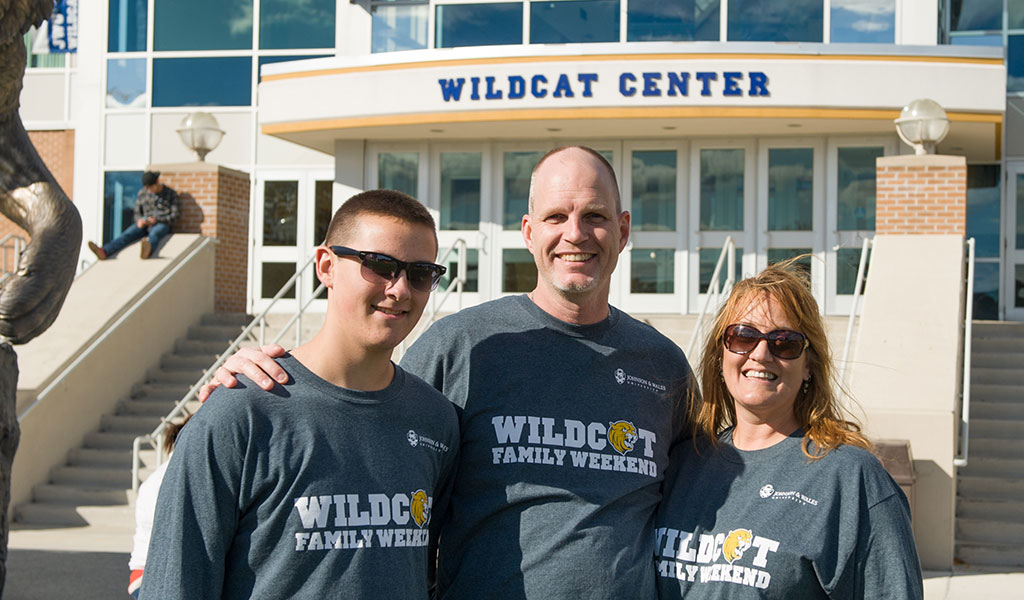Parents with their student smiling for the camera in front of the wildcat center on the Harborside campus