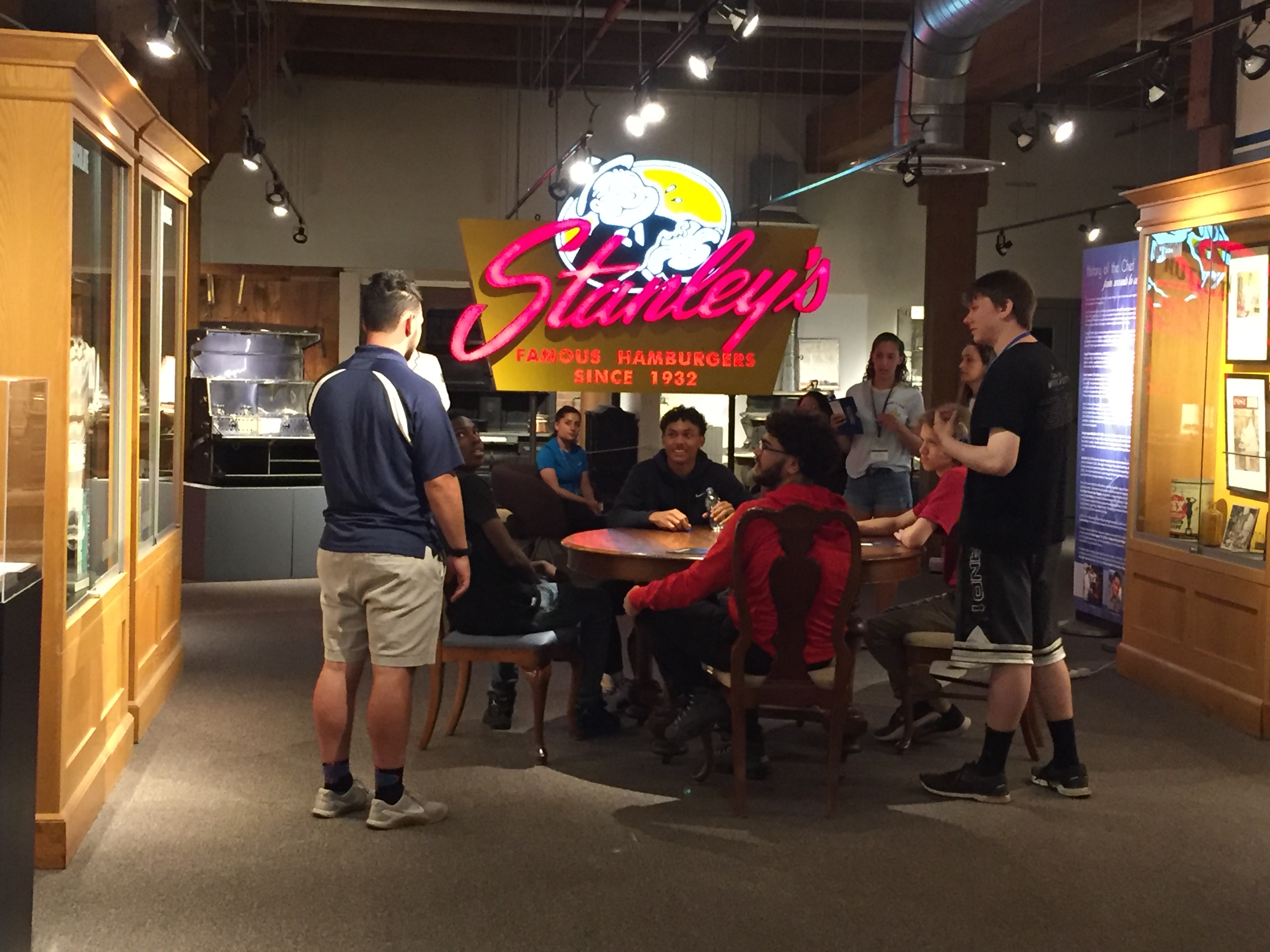Group of students sitting under the Stanley's neon sign
