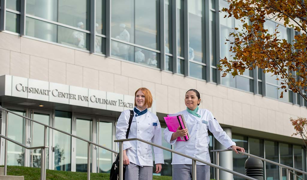 Two culinary students walking down the steps from the Cuisinart Center for Culinary Excellence building