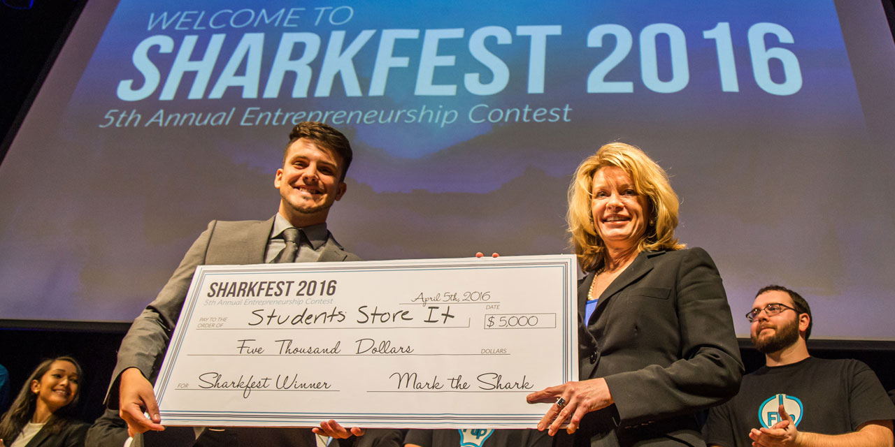 JWU Providence Campus President Mim Runey presents the Sharkfest grand prize to North Miami Campus freshman Thiago Rodrigues.