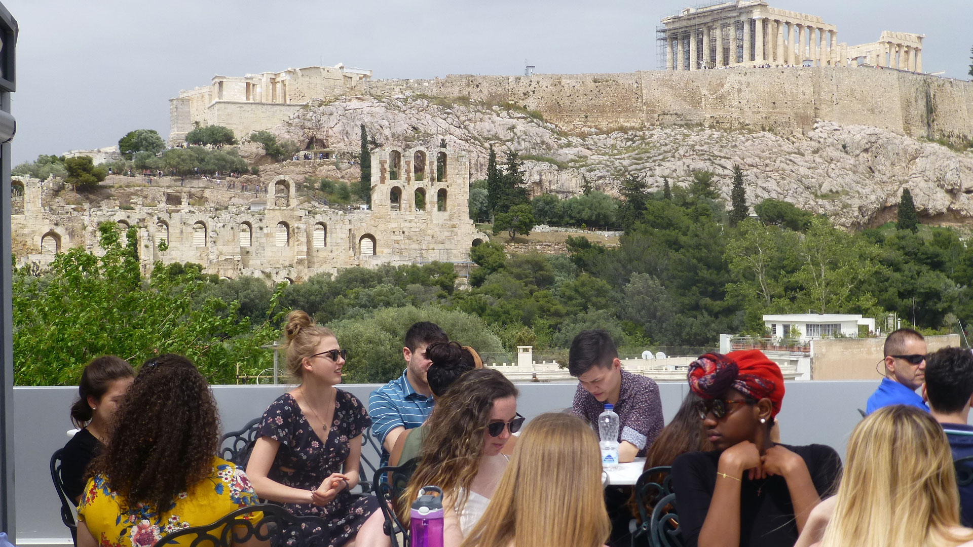Students on a rooftop terrace with the Athens' Acropolis in the background.