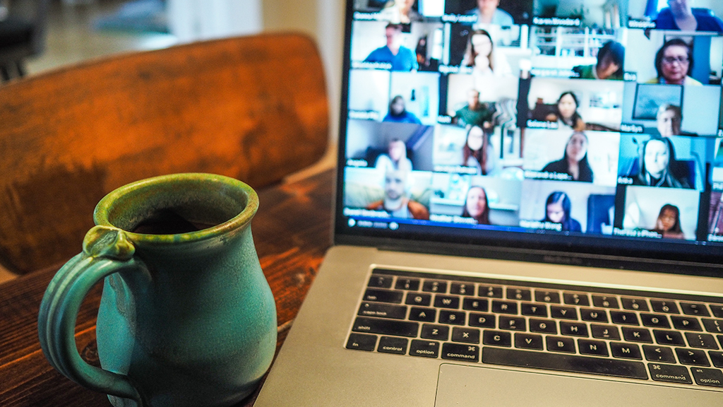 A cup of coffee next to a laptop with a zoom meeting opened