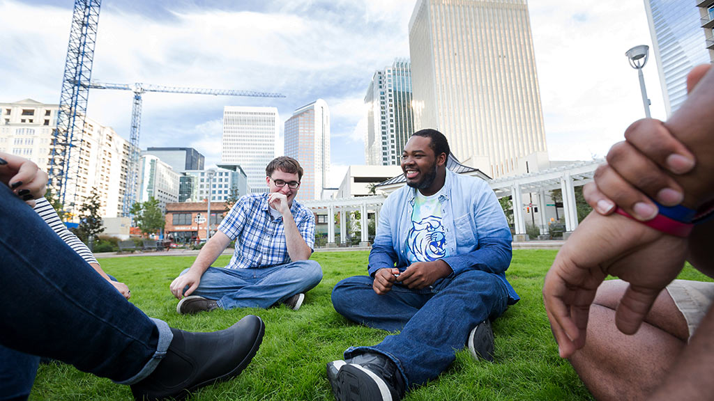 Students sitting in the grass with the Charlotte skyline in the background