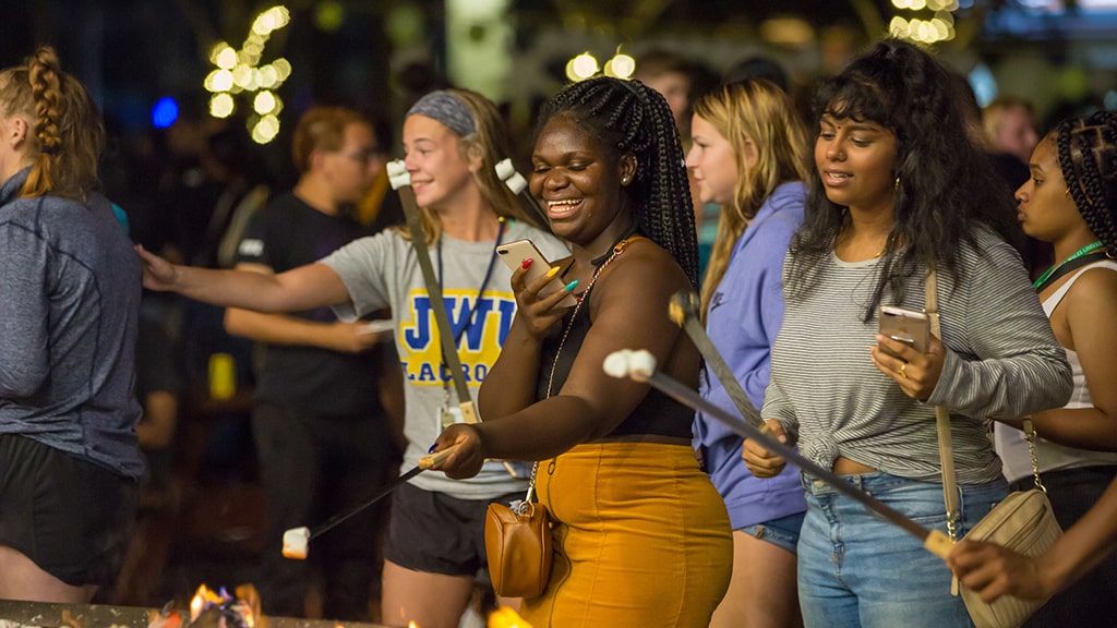 JWU students of different races roast marshmallows together at a student event