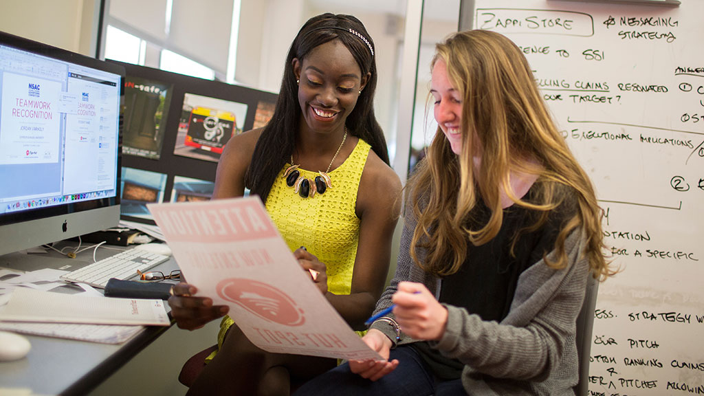 two female students proudly look over their marketing strategy project for a class