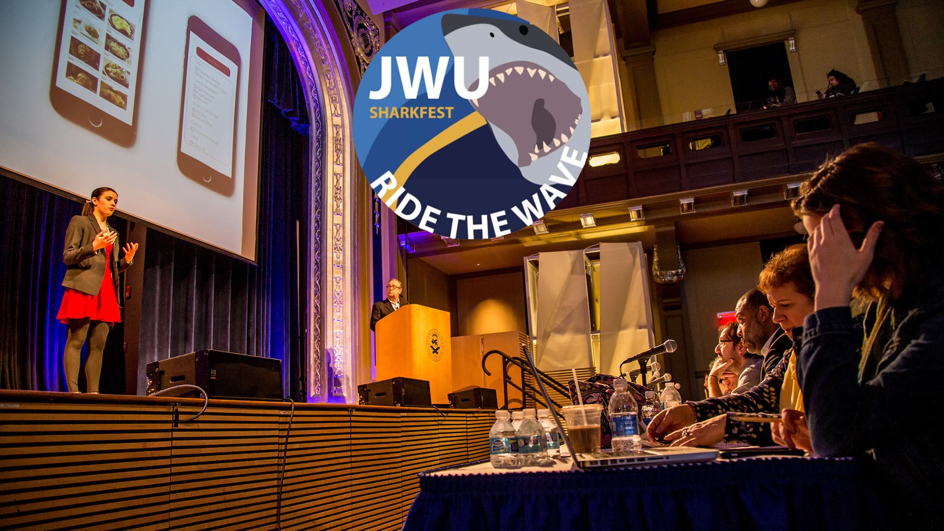 A student presenting on stage at JWU Sharkfest. The JWU Sharkfest logo is in the center.