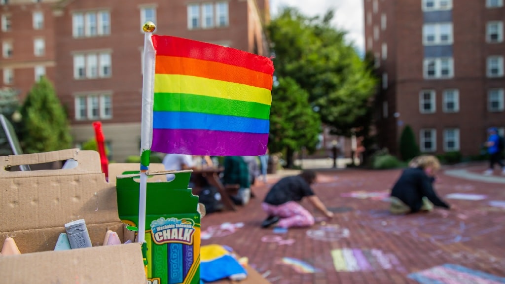 a rainbow flag and two students drawing with chalk
