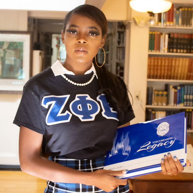 photo of Pheedy Umar '23 wearing a sorority shirt and holding a book