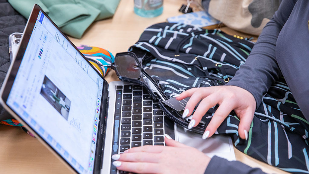 A student on the computer with an article of clothing next to her hands