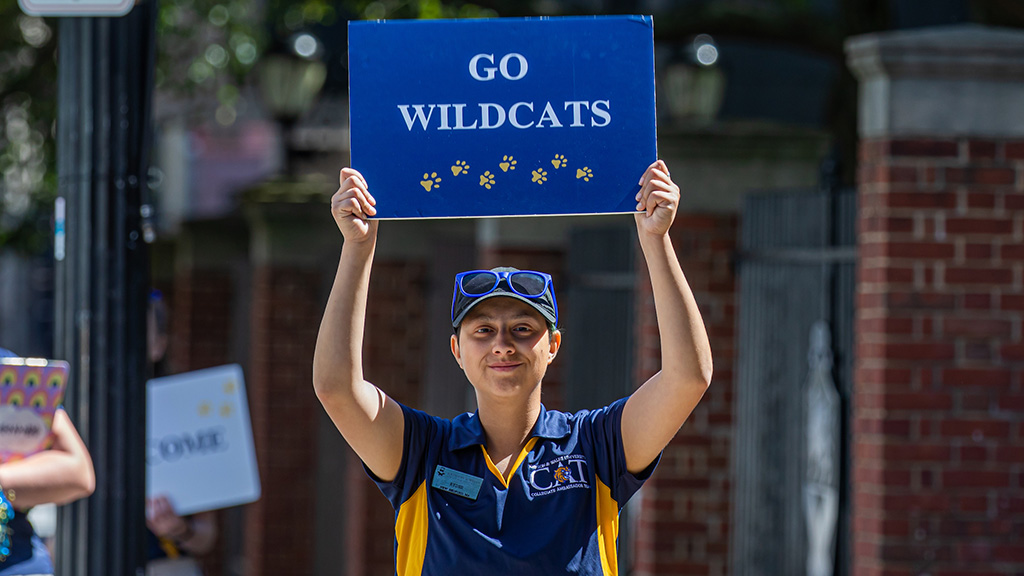 A student holding up a sign that reads "Go Wildcats"