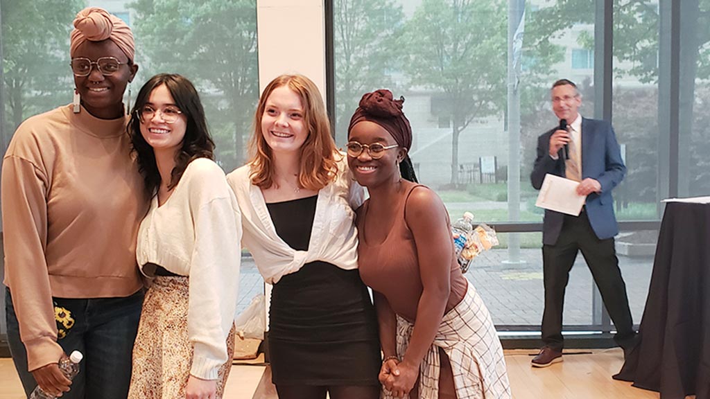 Baking & Pastry Arts majors Crystal Doane, Keely Merrick, Nite' Augustin and Aneesa Larkins pose together in the foreground while JWU Charlotte Campus president Richard Mathiew smiles in the background, announcing their project's award