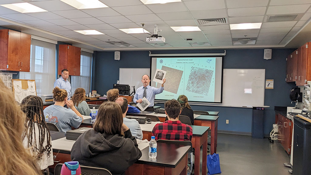 photo of Professor James Desmarais holding up an enlarged photo of a fingerprint during a class presentation on Criminal Justice Experience Day