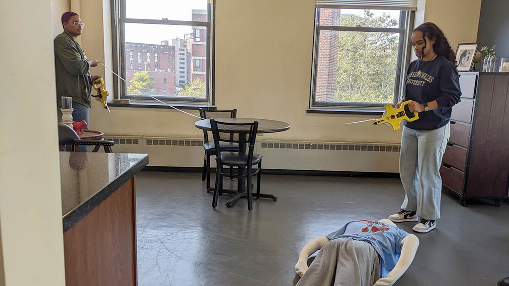 a photo of students in JWU's Crime Scene Room using a measuring wheel to measure the scene