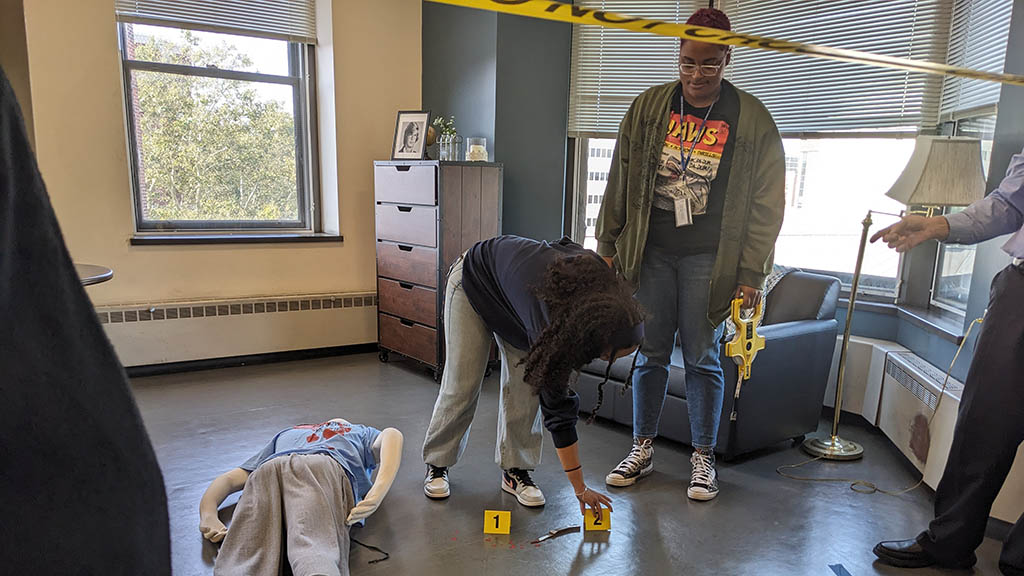 a photo showing students using evidence markers at a mock murder scene in JWU's Crime Scene Room