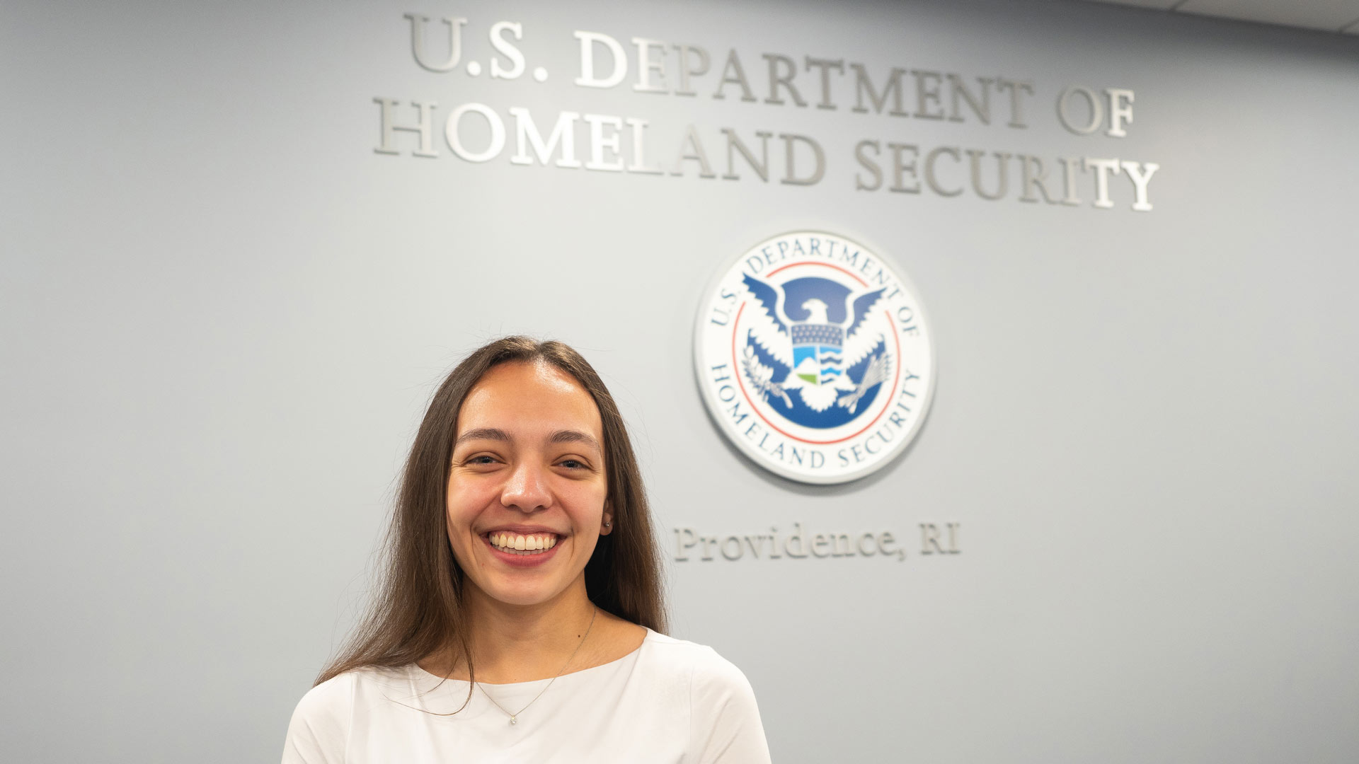 a photo of student Sofia Tamayo '24 posing in front of a Department of Homeland Security wall sign