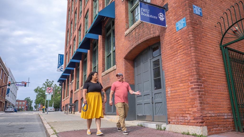 a man and woman hold hands while walking past the JWU bookstore