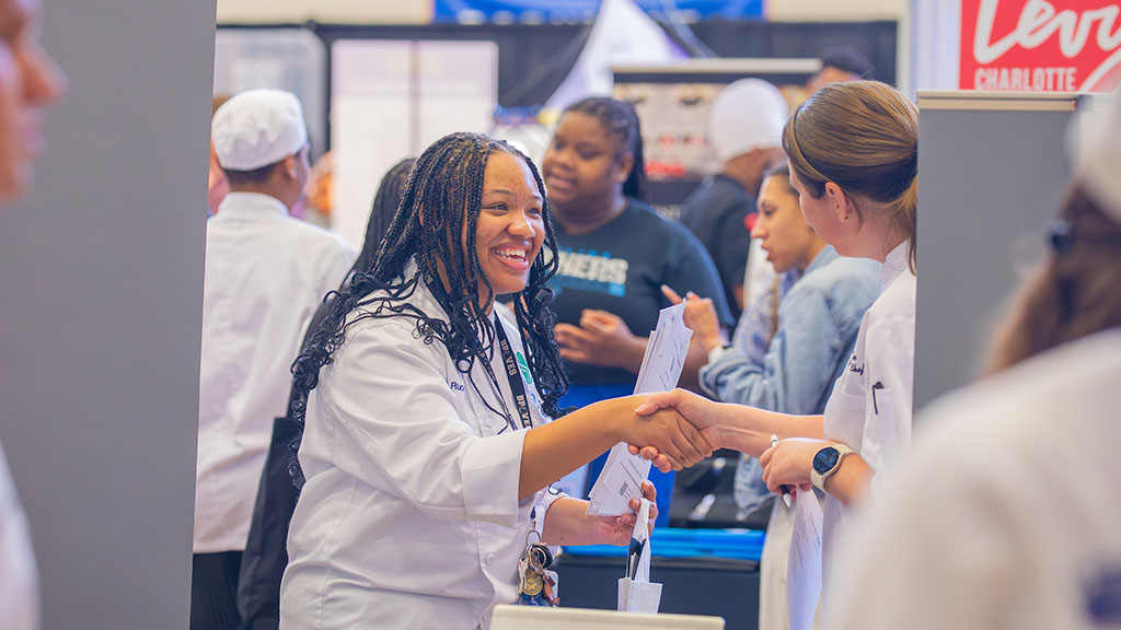 A student on campus shaking hands and networking at the Johnson & Wales career fair.