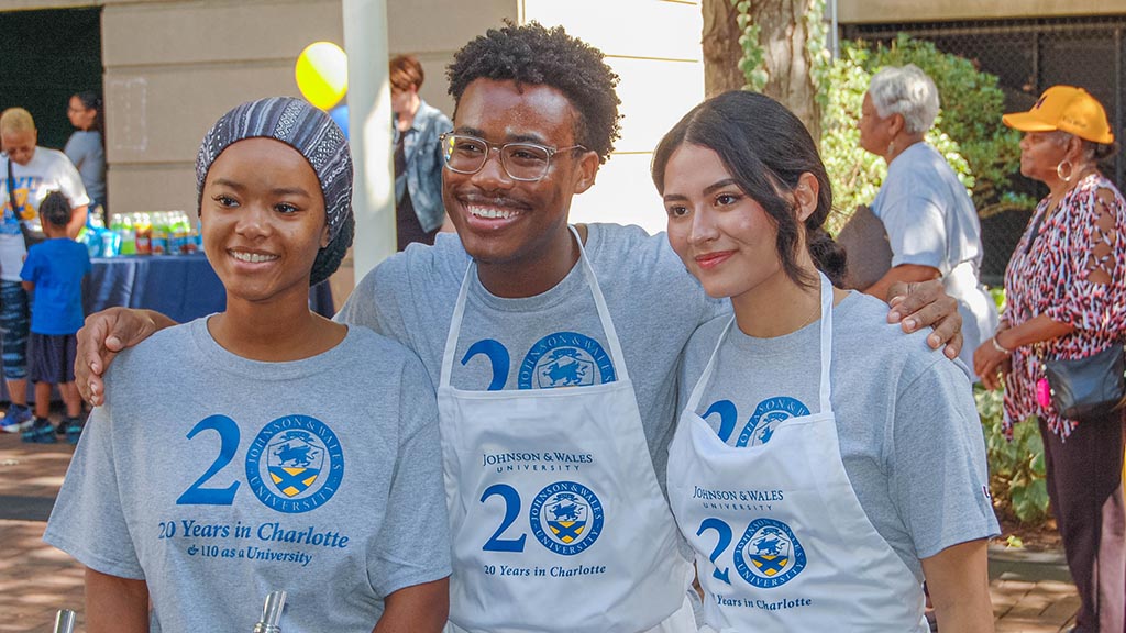 Three students in 20th anniversary t-shirts and aprons during the celebration cookout.