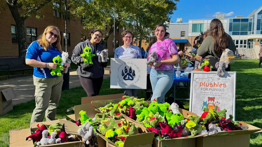 four students pose with JWU P.A.W.S. sign and stuff animals they made for dogs