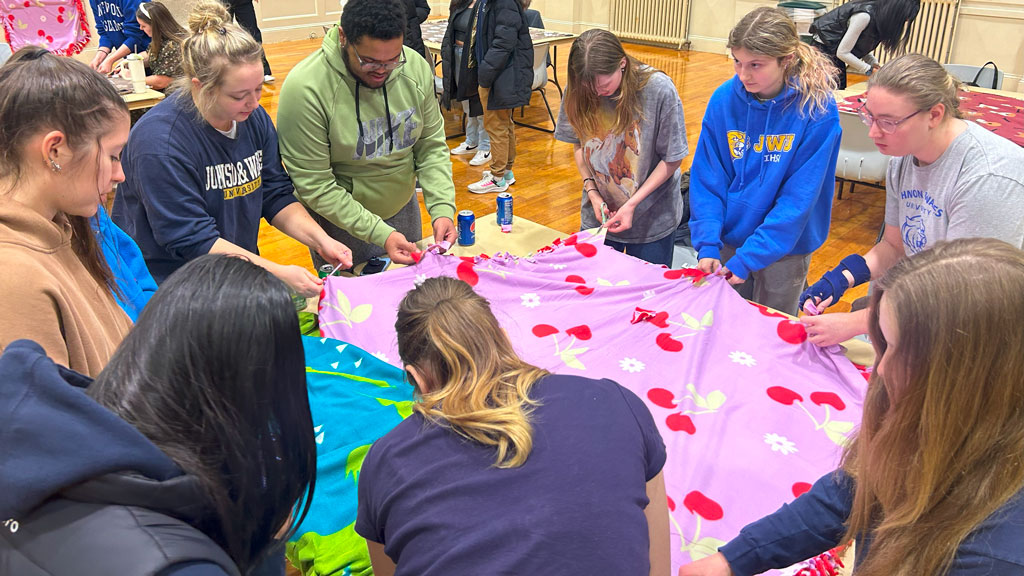 a photo of a group of JWU P.A.W.S. club members concentrating on making tie blankets