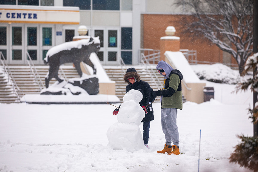 Two students build a snowman on campus.