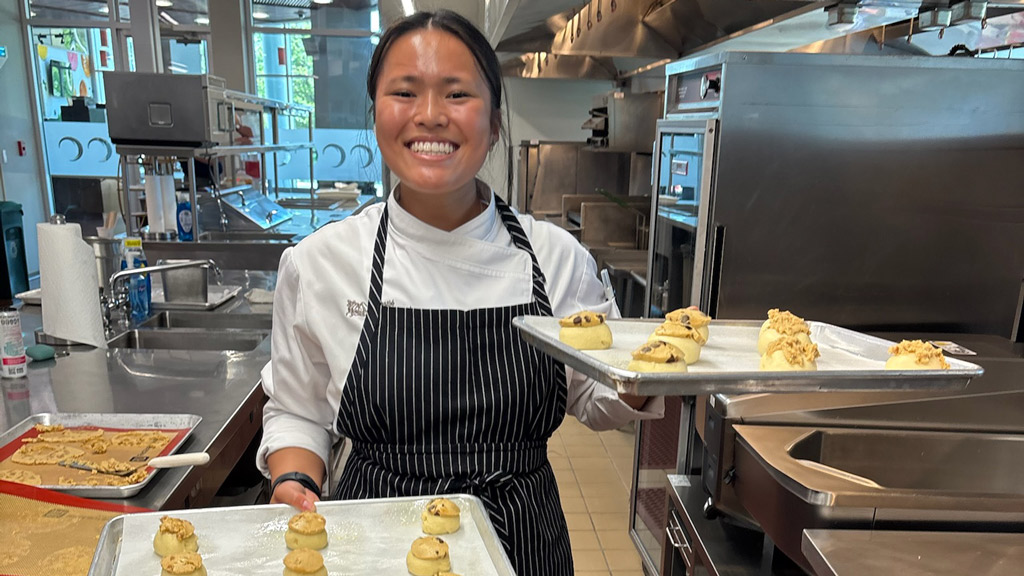 photo of Madison Chan '26 smiling and holding trays of sweets she's just baked