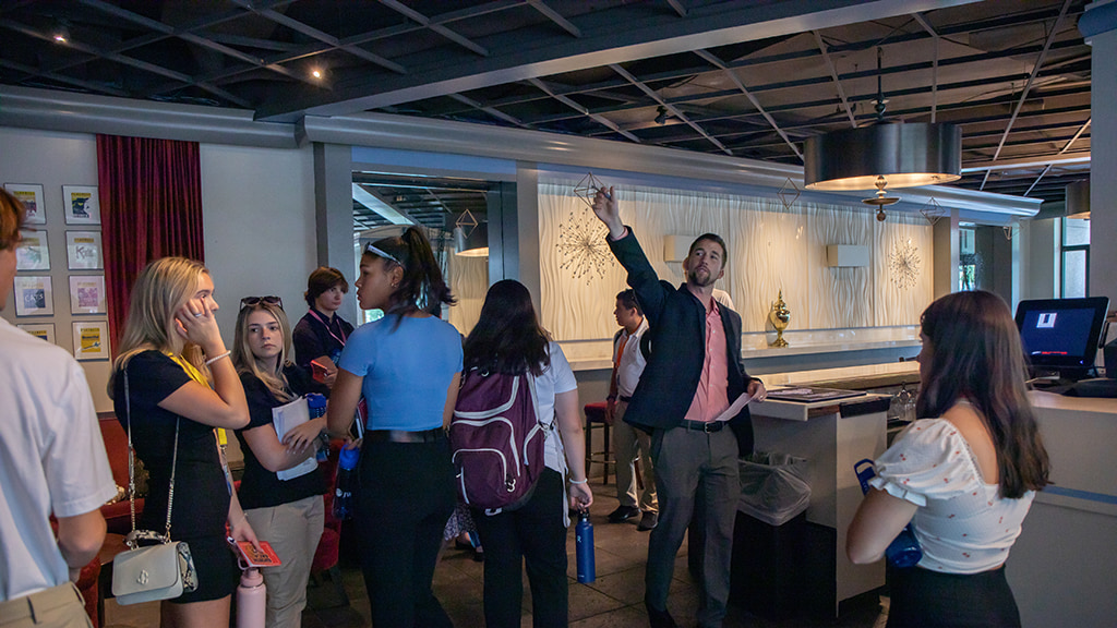 The manager of a hotel points upwards while giving a group of students a tour