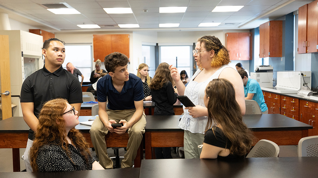 A group of students in a JWU lab sit on desks while talking together
