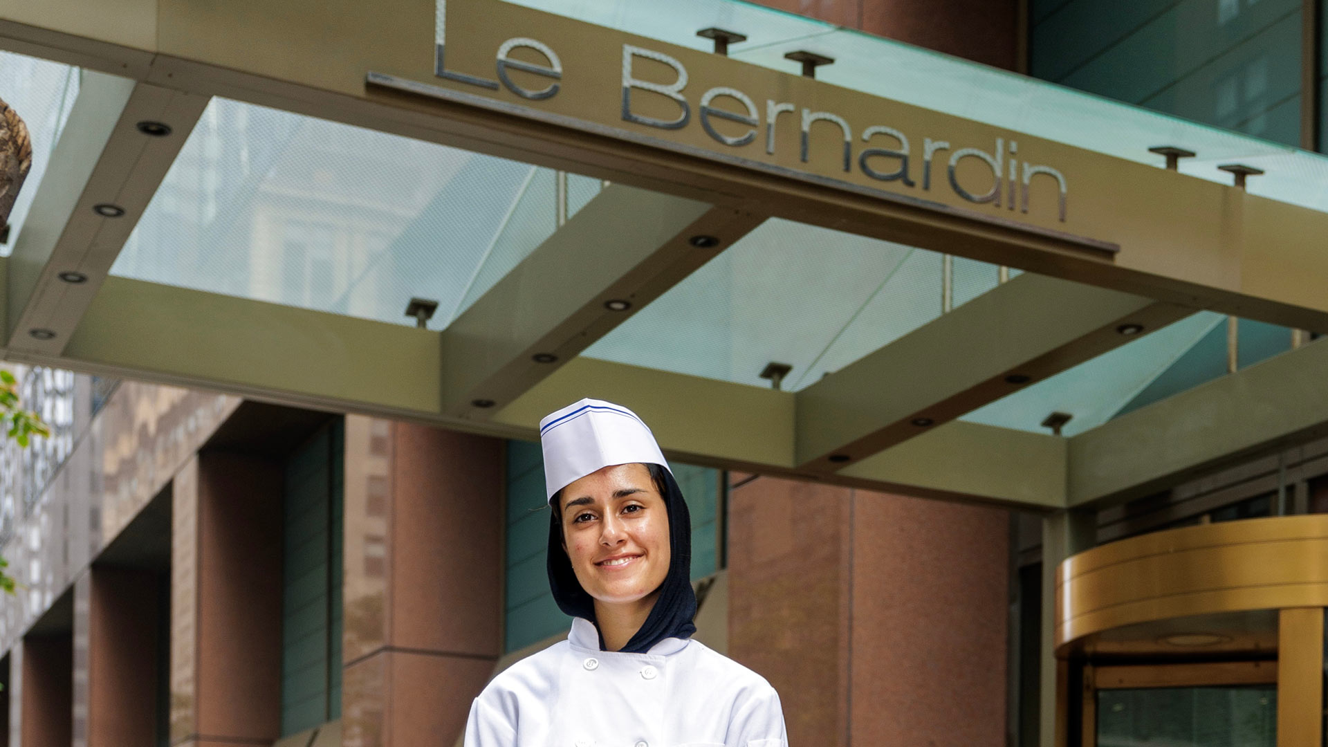 a photo of Fatima Khan '27, in her chef's whites, posing in front of Le Bernardin