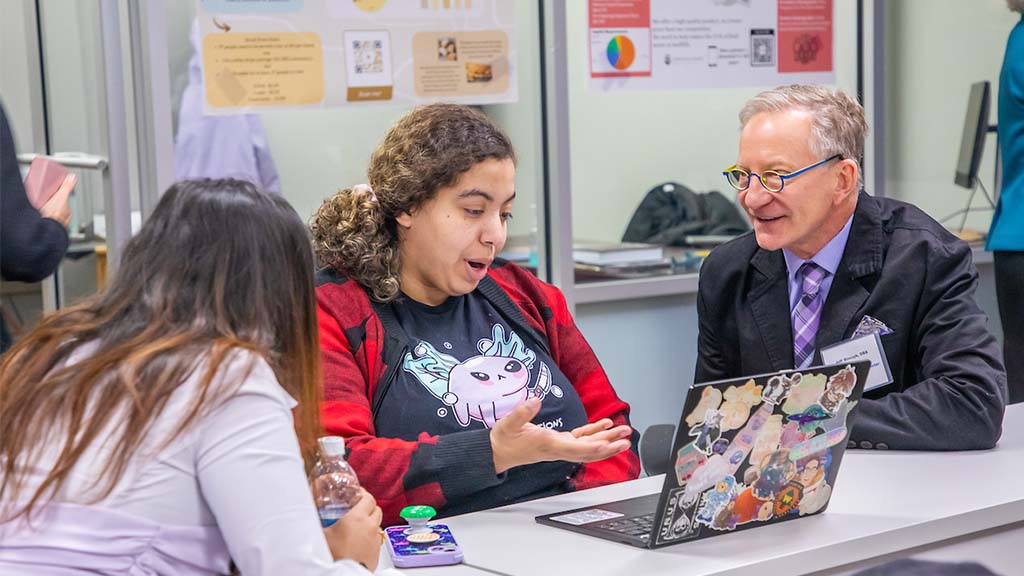 A JWU student speaks while showing something on a laptop to Jeff Binczyk, including another student, during a discussion in the Launch Pad.