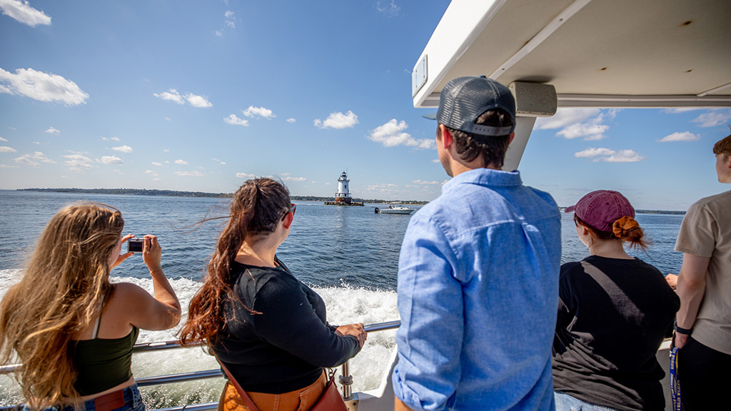 JWU students and a professor on a boat looking at a lighthouse
