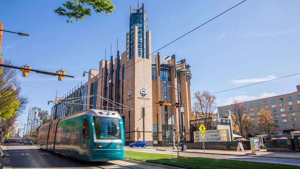 A light rail train passing in front of the Academic Center under a clear blue sky.