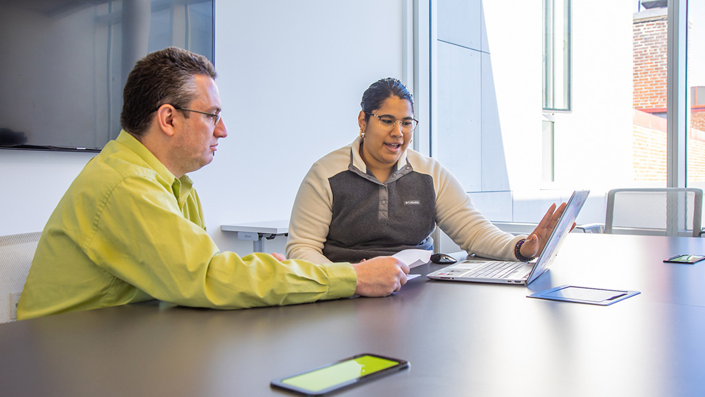 Two people sitting at a table looking at a laptop 