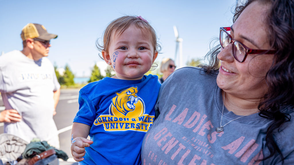 A woman holds a baby with a JWU shirt and facepaint 