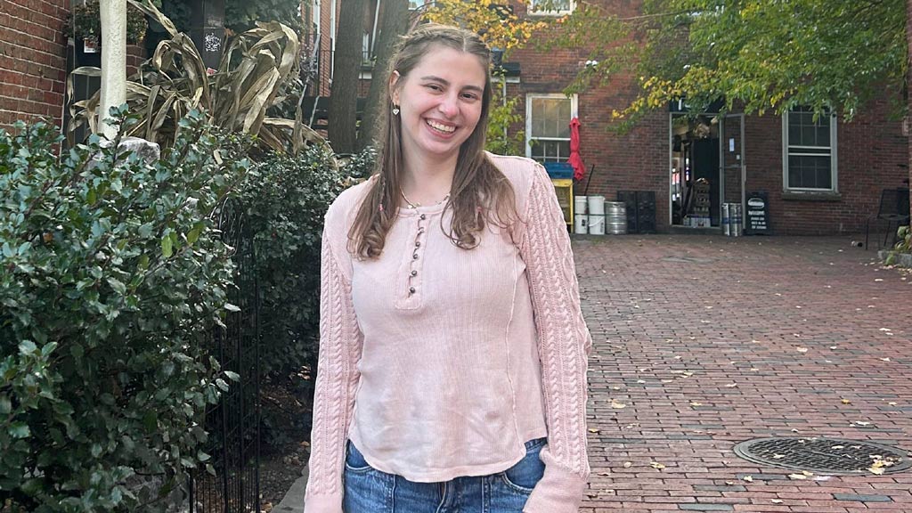 Ava, a student, smiling at the camera in a pink long sleeve