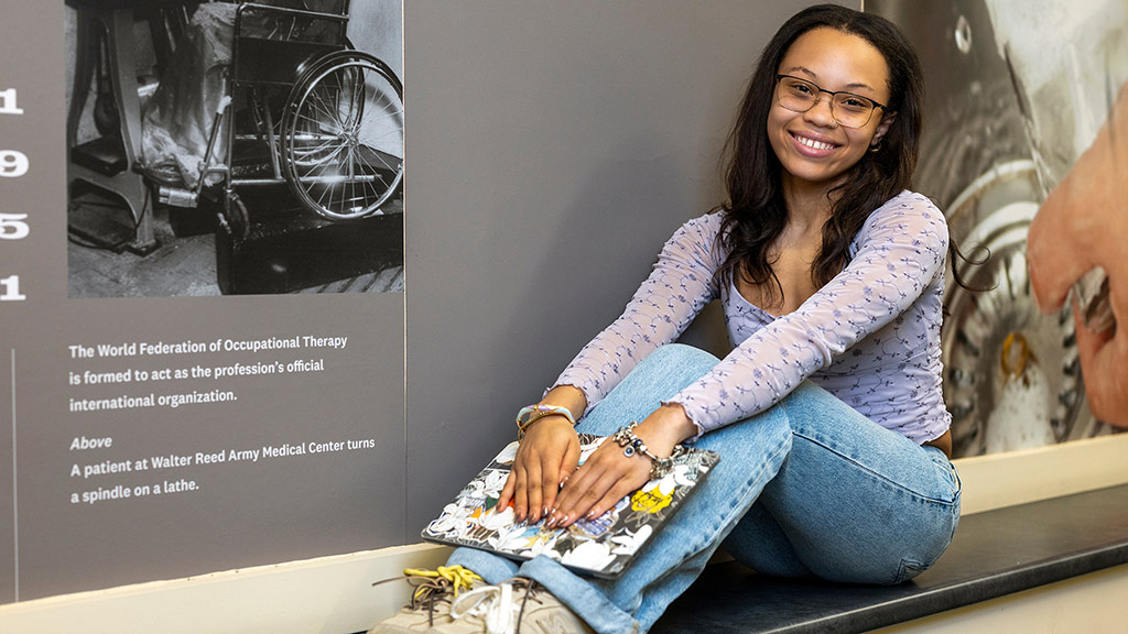 photo of Cora Hicks '27 next to wall art depicting a patient in a wheelchair