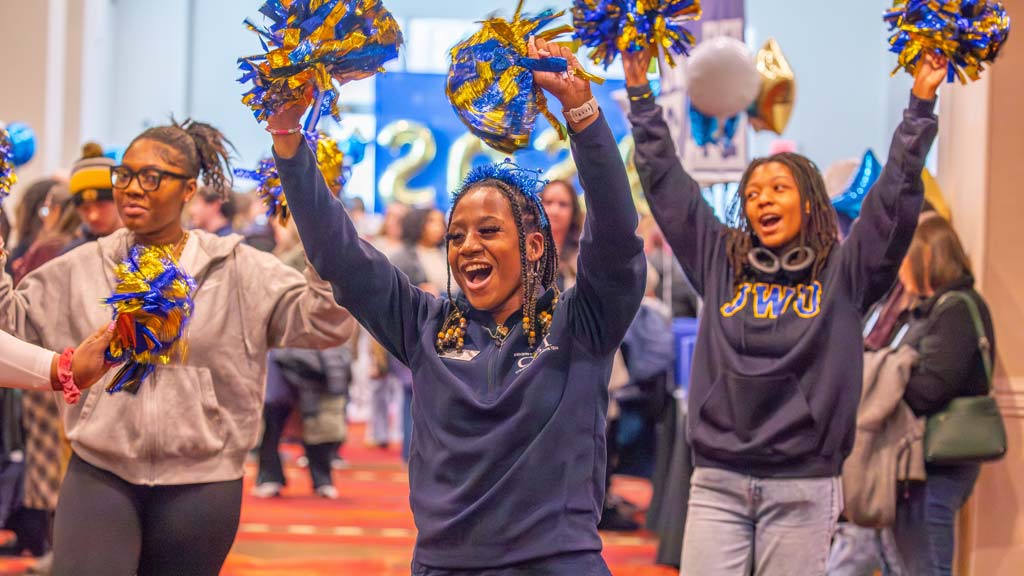 JWU students holding pom poms in the air cheering 