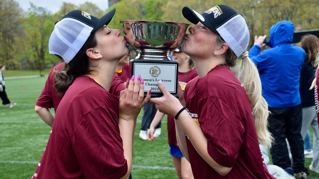 Mila and her teammate kissing their 2024 women's lacrosse championship trophy