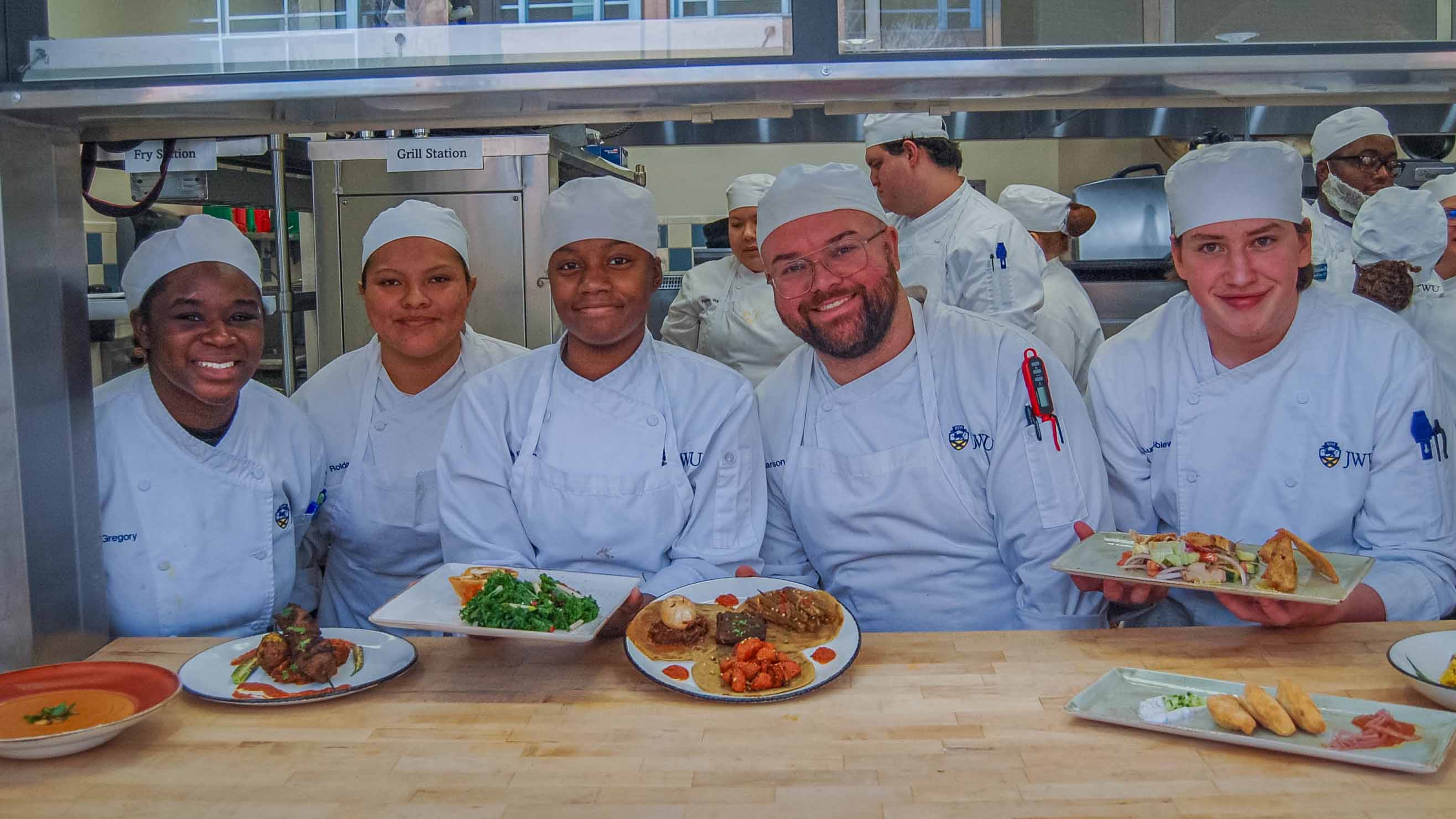 Culinary students in white chef hats and coats in a culinary lab with plated dishes