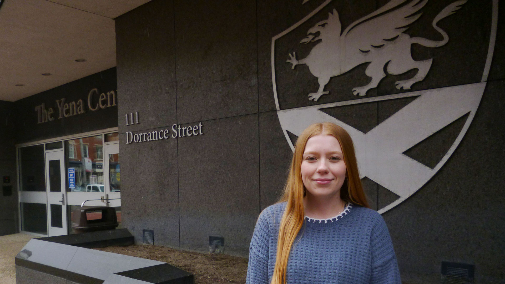 Katie McPartlin '28 poses in front of a Johnson & Wales University seal