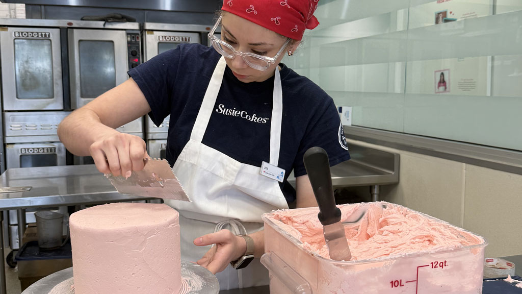 Zoe Bayat '26 frosting a cake for Valentine's day with pink buttercream frosting.