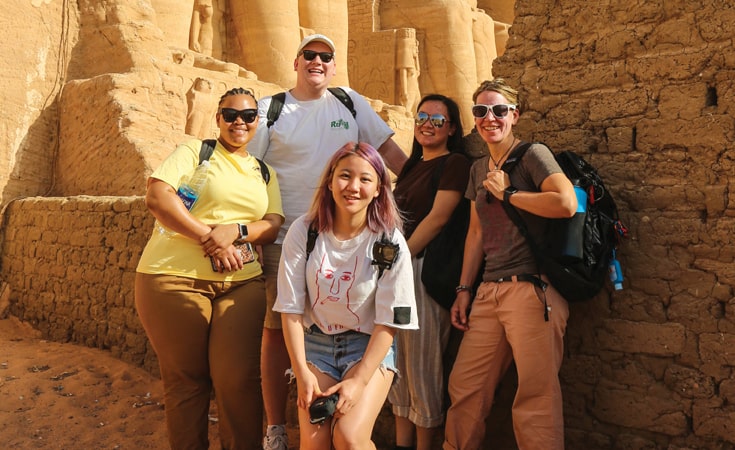 Students and Associate Professor Tiffany Rhodes stand in front of Egyptian pharaohs 